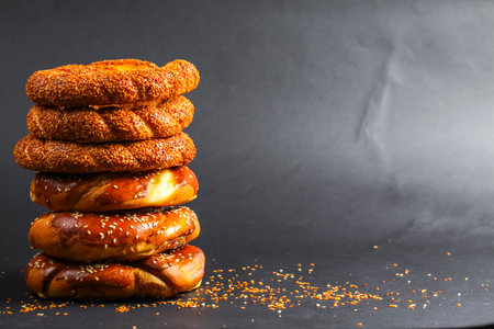 Various types of freshly baked bread rolls are beautifully stacked, showcasing their golden crusts, against a dark backdrop.の写真素材