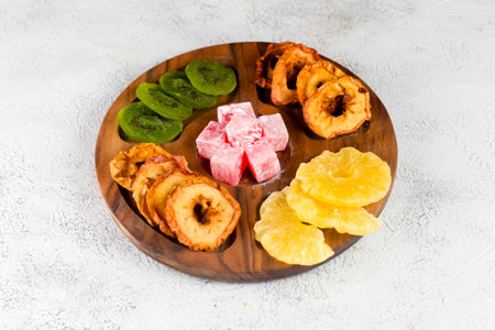 A wooden plate displays an assortment of dried fruits including pineapple, apples, and kiwi, along with colorful confections, creating a vibrant treat display.の写真素材