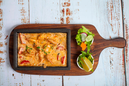 A seafood dish simmering on a cast iron platter, surrounded by a vibrant salad with cucumber, tomato, and lime, showing fresh flavors and colors.の写真素材