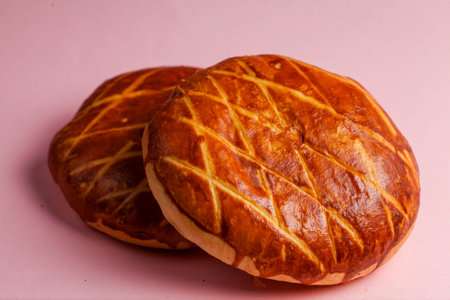 Two round, golden brown bread buns with a crisscross pattern sit on a pink background, showing their crispy texture and inviting appearance.の写真素材