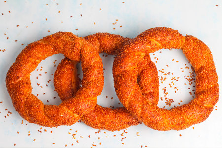 Three warm, golden sesame bagels sit against a light background, sprinkled with seeds. Their crunchy...