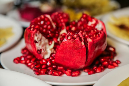 A beautifully cut pomegranate reveals its bright red seeds scattered on a white plate, showing the fruit's juicy interior and inviting appearance.の写真素材