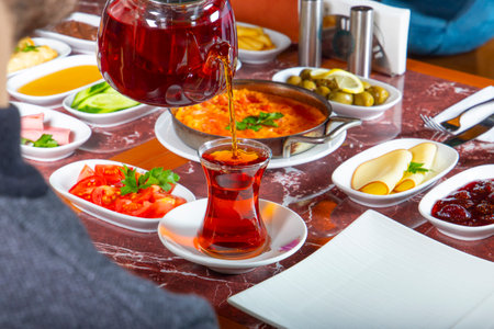 Warm tea is poured into a glass as a spread of diverse dishes, including pickles and fresh vegetables, fills the dining table for a satisfying meal.の写真素材