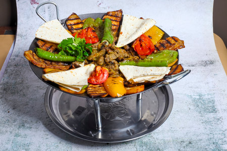 A vibrant platter filled with grilled meat, assorted vegetables, and tortillas sits on a silver stand, showing rich colors and appetizing textures.の写真素材