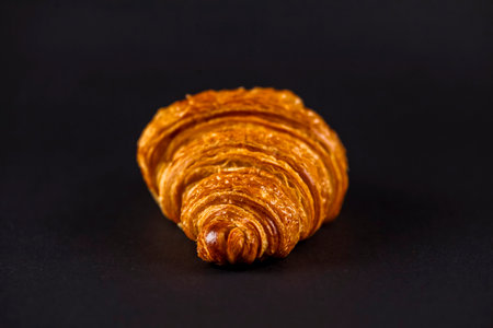 A perfectly baked croissant sits against a dark backdrop, showcasing its golden layers and flaky texture, highlighting the craftsmanship in pastry making.の写真素材