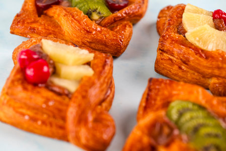 Colorful fruit pastries are arranged neatly, showing a variety of toppings like pineapple, kiwi, and cherries.の写真素材