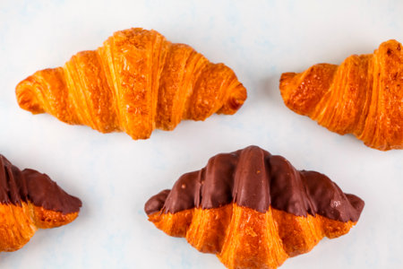 Flaky, golden croissants are arranged on a light background, showcasing a variety of classic and chocolate-dipped options ready to savor.の写真素材