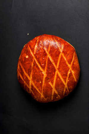 This round bread features a glossy, golden-brown crust and a unique cross pattern. It sits on a...