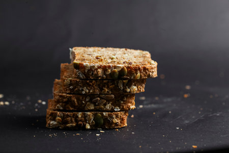 Slices of multigrain bread stacked neatly, showing a mix of seeds and grains against a dark backdrop, highlighting its wholesome texture and appeal.の写真素材