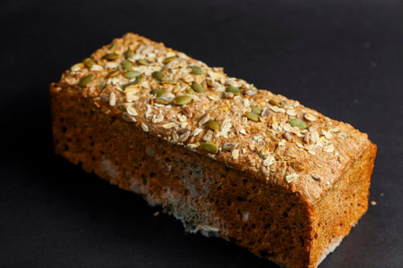 Freshly baked seeds and nut bread topped with pumpkin seeds sits on a dark surface, highlighting its...