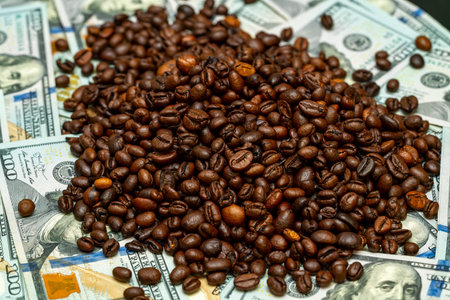 A pile of roasted coffee beans rests on a surface of various banknotes. The rich brown color of the...