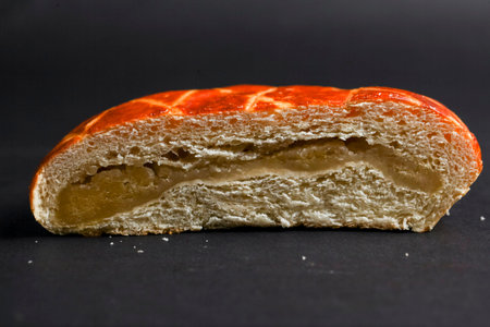 A freshly baked sweet roll is displayed, revealing a smooth golden filling inside. The soft bread...