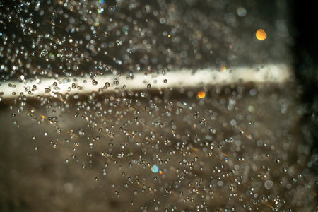 Tiny water droplets cluster on a glass surface, reflecting colorful lights from the surroundings while the ground remains wet after a recent rain shower.の写真素材