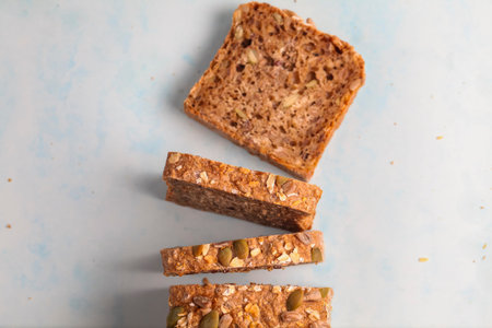 Whole grain bread is sliced and arranged on a blue surface, highlighting its hearty texture and...
