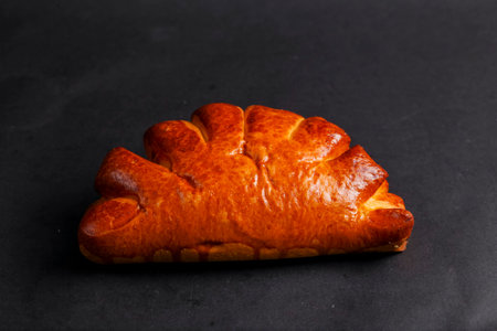 Golden brown pastry sits on a dark surface, showing a flaky texture and inviting sheen. Ideal for breakfast or a snack any time of day.の写真素材