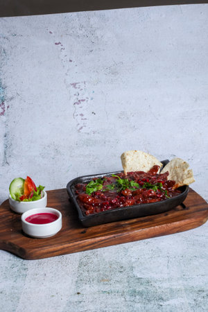 A flavorful dish sits on a wooden board, featuring a rich red sauce with tortillas and fresh salad, garnished with green herbs for an appetizing look.の写真素材