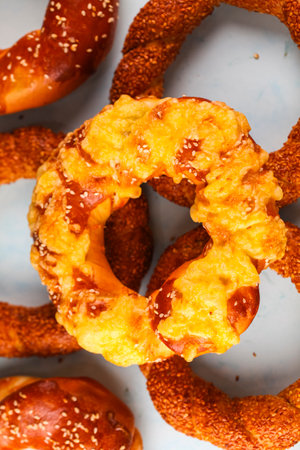Freshly baked soft pretzels feature a cheesy topping and sesame seeds. These golden treats are arranged on a blue background, inviting onlookers to indulge.の写真素材