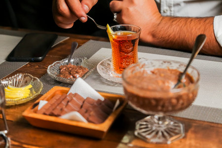 Sweet treats and aromatic tea are served at a wooden table, with a hand stirring a drink while plates of dessert await savoring in a warm atmosphere.の写真素材