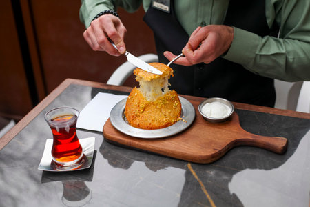 A server uses a knife to slice through a golden-brown cheese-filled pastry at a restaurant table,...