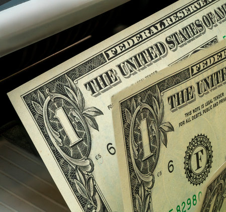 A one-dollar bill is partially emerging from a currency machine, showing the printing process. The intricate details of the bill are clearly visible.の写真素材