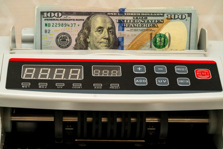 A counting machine processes a one hundred dollar bill, displaying the amount. The device is indicated to ensure accurate cash management.の写真素材