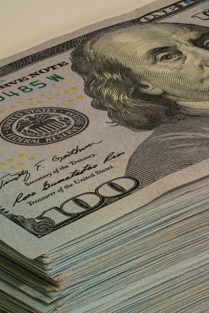 Stacks of hundred dollar bills are neatly arranged, showing the intricate design and detail of the currency. Soft lighting highlights the green hues.の写真素材