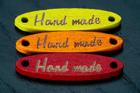 Three vibrant wooden tags are displayed in a row, showing the words Hand made in three different...