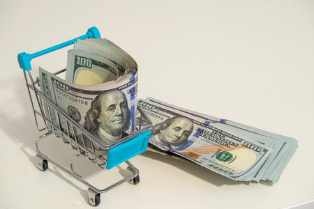 A shopping cart contains neatly stacked bundles of cash, symbolizing wealth and commerce. One bundle spills out beside it, enhancing the theme of abundance.の写真素材