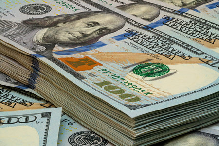 A detailed view of neatly stacked hundred dollar bills showing their vibrant colors and intricate...