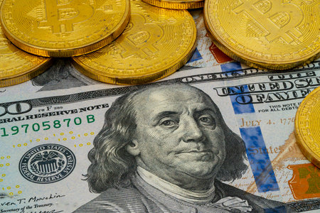 A collection of golden cryptocurrency coins sits next to a hundred-dollar bill of Benjamin Franklin, highlighting the link between old and new money.の写真素材