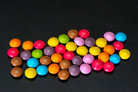 A variety of brightly colored candies are arranged in a playful pattern on a dark surface, showing their vibrant hues and enticing appearance.の写真素材