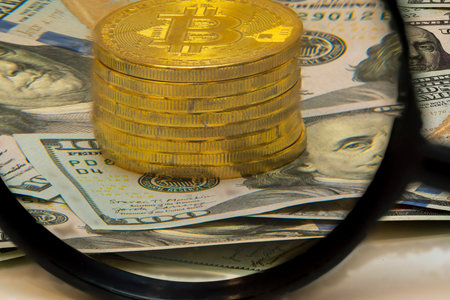 A stack of shiny Bitcoin coins is positioned prominently atop a spread of US dollar bills, with a...