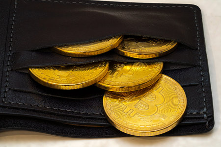 Display shows a black wallet partially opened to reveal shiny gold Bitcoin coins inside, symbolizing digital currency and the future of finance.の写真素材
