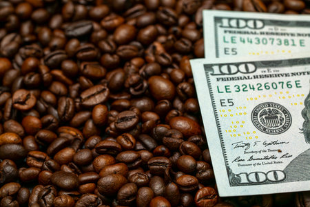 Dark roasted coffee beans spread out with two hundred dollar bills placed on top, creating a rich...