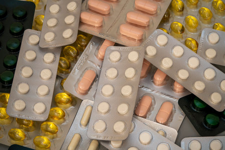 Various types of capsules and tablets lay scattered on a surface, featuring different colors and...