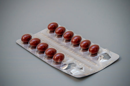 A blister pack containing brown capsules rests on a smooth gray surface. Each capsule is neatly...