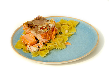 A plate features a portion of baked salmon atop colorful bowtie pasta, showcasing a blend of flavors and textures in a well-arranged presentation.の写真素材