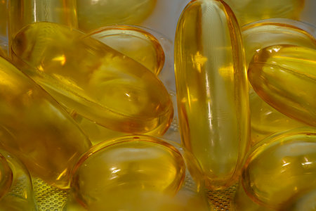 Close-up view of yellow gel capsules used for dietary supplements, displayed on a textured surface with soft lighting, highlighting their smooth texture and transparency.の写真素材