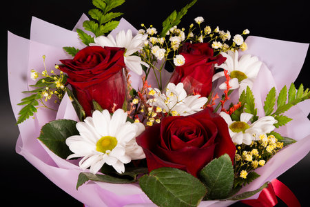 This lovely bouquet features vibrant red roses and delicate white daisies surrounded by lush greenery, elegantly wrapped for a special occasion.の写真素材
