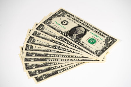 A neat stack of one dollar bills lies on a plain surface, showing their design and detailed...