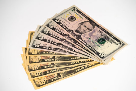 A stack of five and ten dollar bills is neatly arranged on a plain surface, showing crisp notes with...