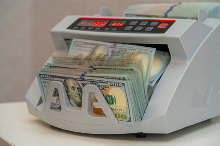 A money counting machine processes stacks of hundred-dollar bills in a financial office during the...