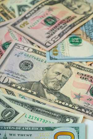 A collection of banknotes in different denominations is scattered across a flat surface, showing...