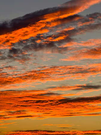 The sky transforms at dusk with vivid orange and purple clouds. Sunlight fades, creating a serene and colorful scene over the horizon.の写真素材