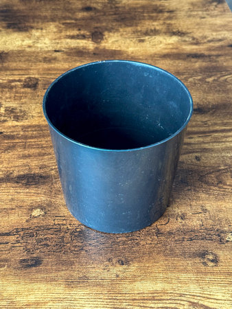 A black round pot is placed on a wooden table. The pot is empty and has a smooth surface. The table shows a natural wood grain pattern and color.の写真素材