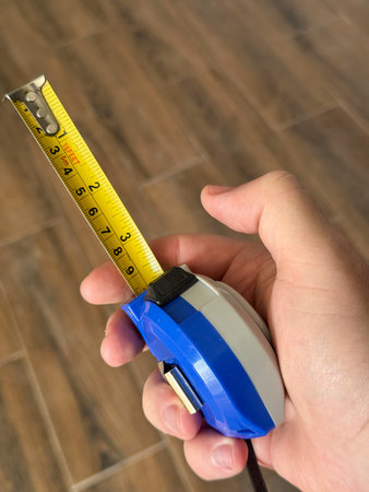 A person holds a measuring tape in their right hand. The tape is extended partially and shows clear...