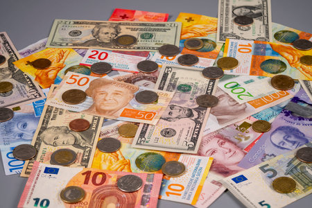 Different banknotes and coins are laid out on a flat surface. The cash includes various currencies...