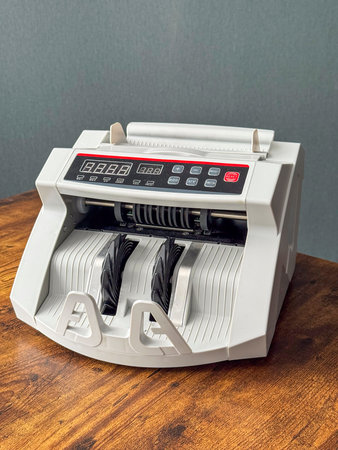 A counting machine sits on a wooden table in a business space. The device has screens and buttons...