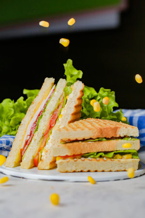A plate holds stacked sandwiches with layers of meat and vegetables. Green lettuce and corn pieces...