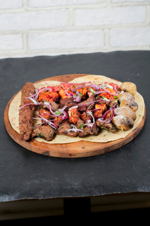 A large wooden plate holds a variety of grilled meats and vegetables. Skewers of meat sit alongside...